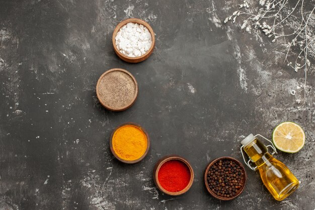 Top view appetizing food bowls of colorful spices bottle of oil and lemon next to the tree branches