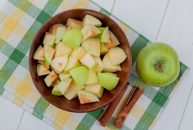 Free photo top view of apple cubes in bowl and whole one with cinnamon on plaid cloth and wooden