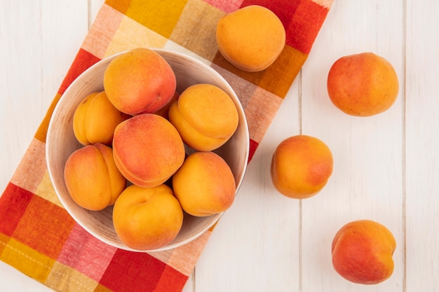 Top view of apricots in bowl on plaid cloth and on wooden background