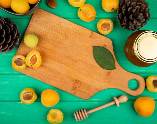 Top view of apricots and leave on cutting board with pinecones and peach jam on green background