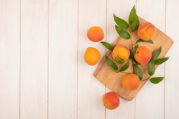 Top view of apricots and leaves on cutting board and on wooden background with copy space