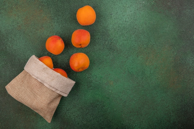 Free Photo top view of apricots spilling out of sack on green background with copy space