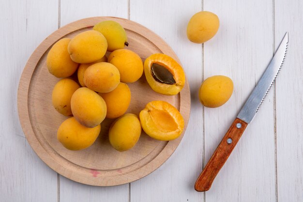 Top view of apricots on a stand with a knife on a white surface