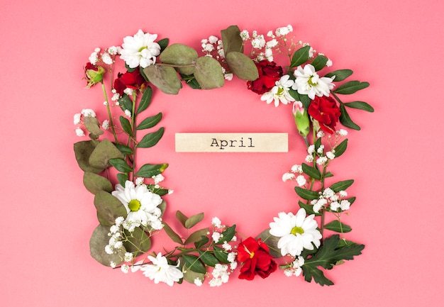 Top view of april text middle of colorful flower wreath against peach surface