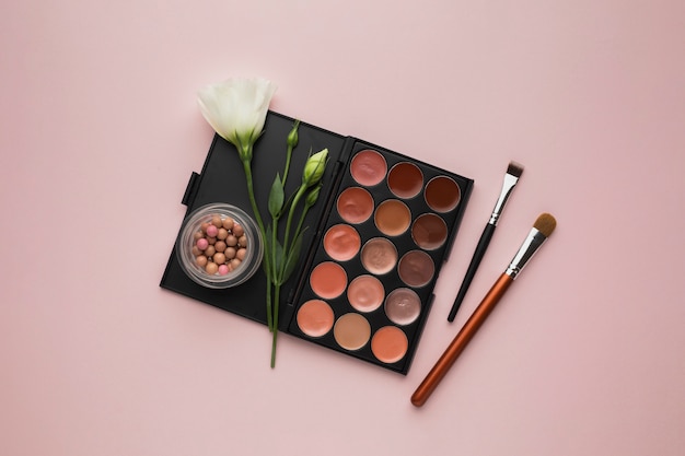 Top view arrangement with make-up palette and pink background