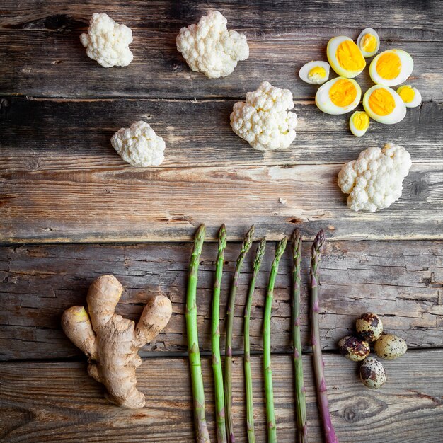 Top view asparagus with ginger, eggs, cauliflower on dark wooden background.