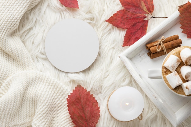 Top view of autumn leaves and cup of hot cocoa on tray with marshmallows