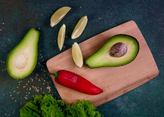 Free Photo top view avocado halves on a blackboard with red pepper lemon and lettuce on a dark green background