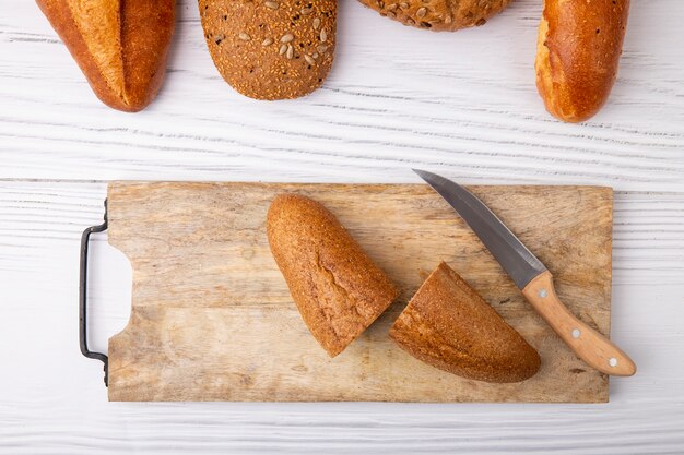 Top view of baguette cut in half with knife on cutting board on wooden background