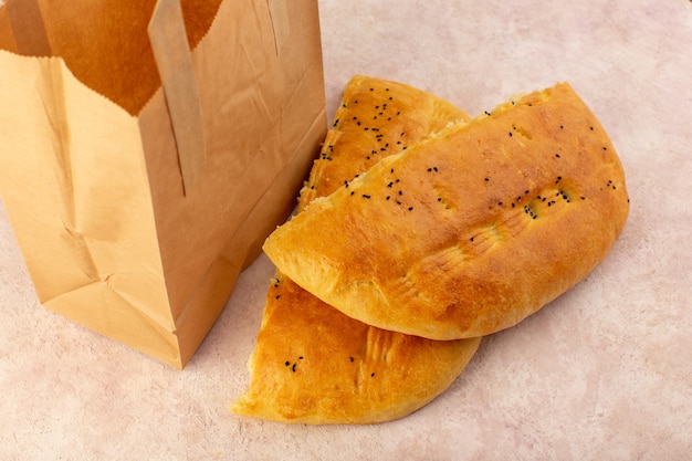 A top view baked bread hot tasty fresh half sliced inside and outside paper packages on pink