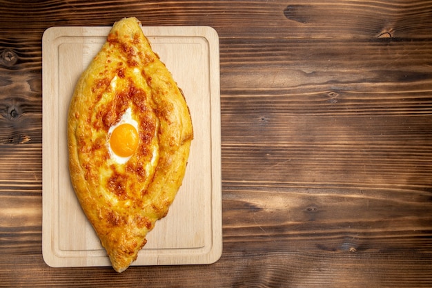 Free photo top view baked bread with cooked egg on brown wooden desk bread bun food egg breakfast dough