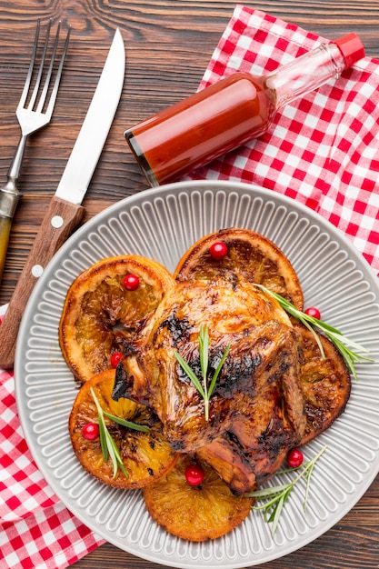 Top view baked chicken and orange slices on plate with cutlery and sauce