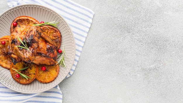 Top view baked chicken and orange slices on plate with kitchen towel and copy-space