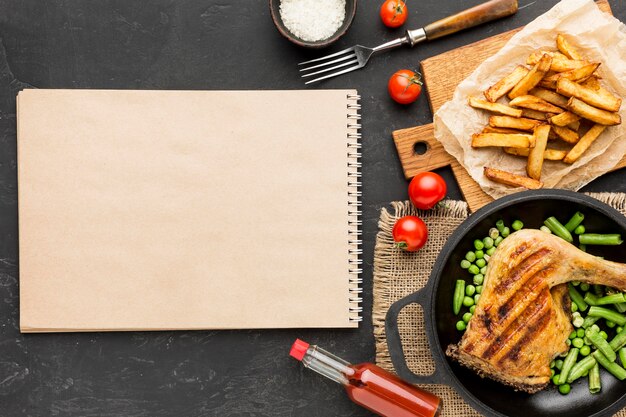 Top view baked chicken and pea pods in pan with potatoes and blank notebook