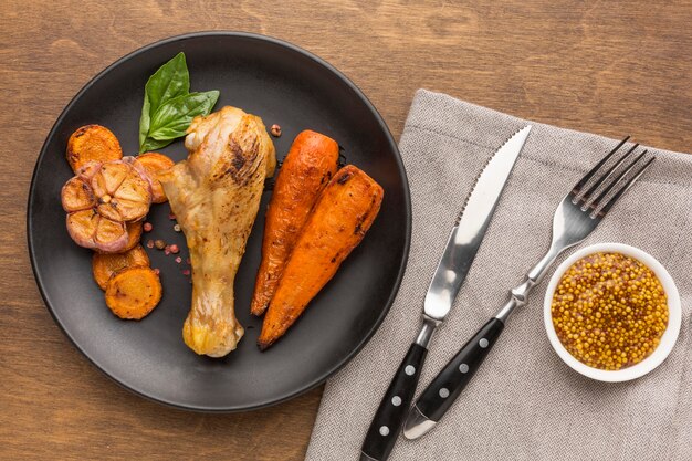 Top view baked chicken and veggies on plate with cutlery and dijon mustard