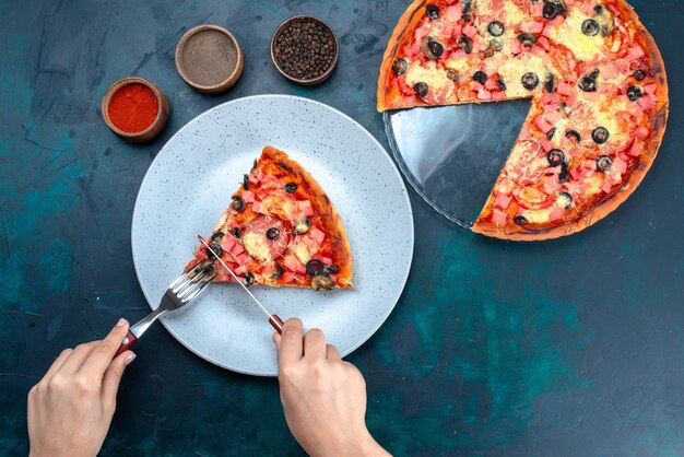 Top view baked delicious pizza with olives sausages and cheese female eating it on blue desk.