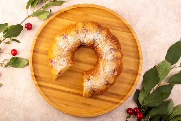 A top view baked fruit cake delicious sliced with red cherries inside and sugar powder on wooden round desk on pink