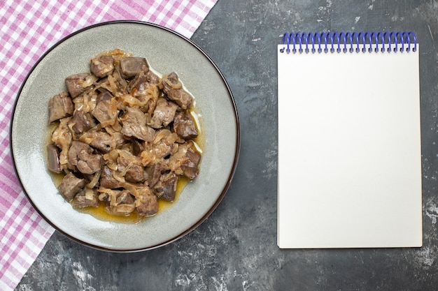 Free photo top view baked liver and onion on oval plate on tablecloth and empty notebook