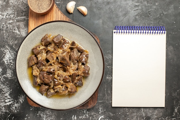 Free photo top view baked liver and onion on plate black pepper on chopping board garlic notepad