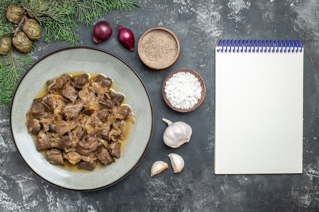 Free photo top view baked liver and onion on plate pine tree branch sea salt and pepper garlic and empty notebook