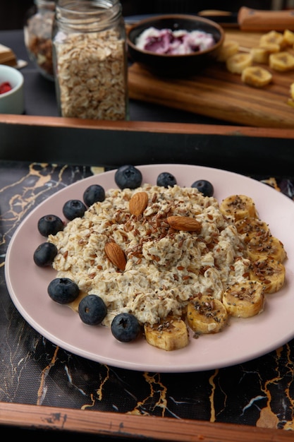 Top view of banana blackthorn almond flax oatmeal with crispbreads and glass of milk in tray on black background