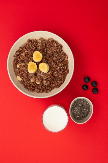 Top view of banana walnut oatmeal in bowl with glass of milk bowl of chia seeds and blackthorn berries on red background