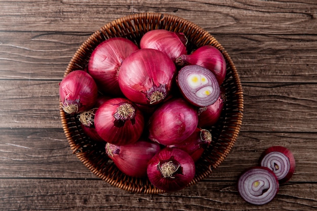 Top view of basket full of whole and cut red onions on wooden background with copy space