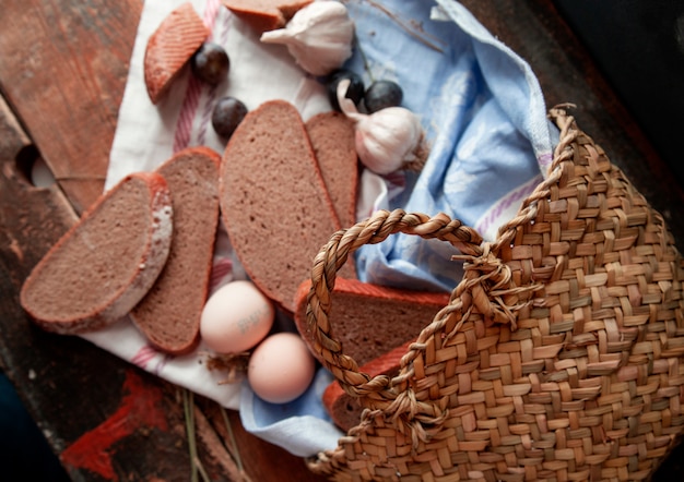 Top view basket with bread slices eggs, plum and garlics around on a wooden table.