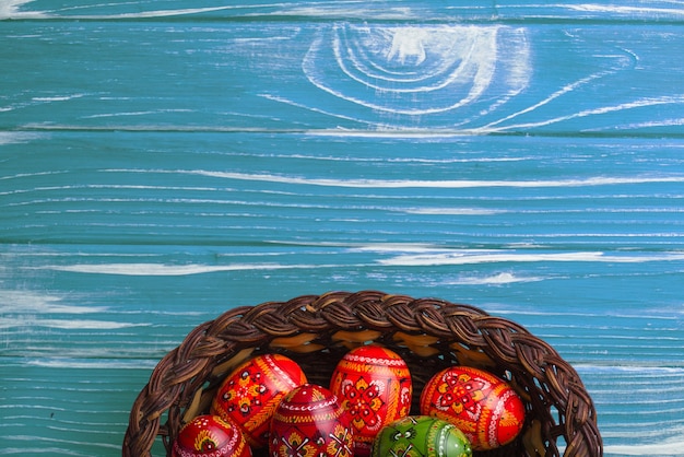 Free photo top view of basket with colorful easter eggs on wooden background