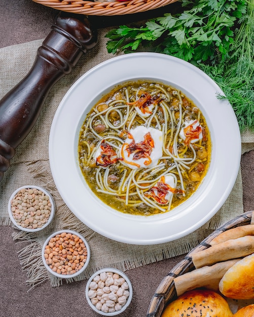 Free photo top view bean soup with grilled onion noodles beans sour cream black pepper and greens on the table