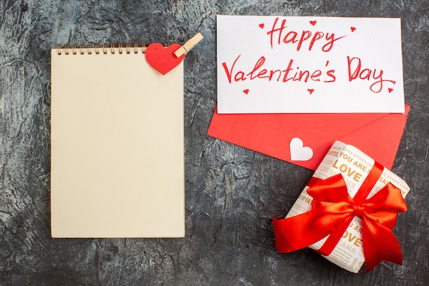 Top view of beautiful gift box tied with red ribbon for Valentines Day and notebook on icy dark background