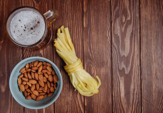 Top view of beer snacks almond in a bowl and string cheese with mug of beer on rustic wood with copy space