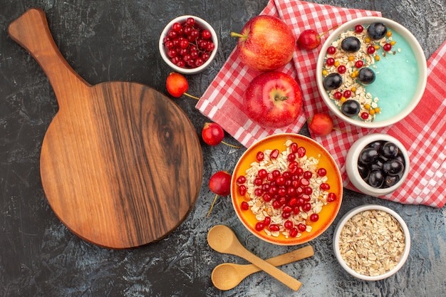 Top view of berries spoons apples colorful berries oatmeal pomegranate the cutting board