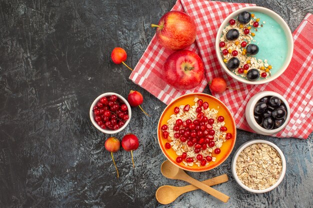 Top view of berries spoons red currants cherries grapes apples pomegranate oatmeal in bowl