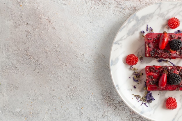 Top view berry cake slices with red creamy icing and fresh berries on white surface