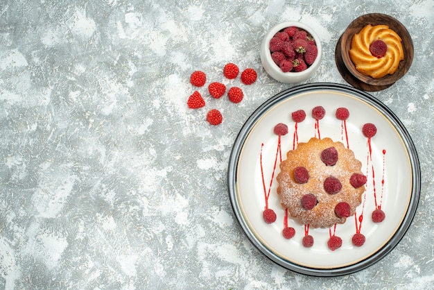 Top view berry cake on white oval plate bowl with raspberries biscuit on grey surface free space