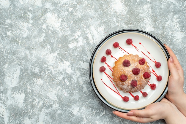 Top view berry cake on white oval plate in female hand on grey surface free place