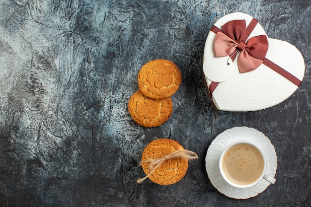 Top view of best surprise with beautiful gift box and a cup of coffee cookies for beloved one on icy dark surface