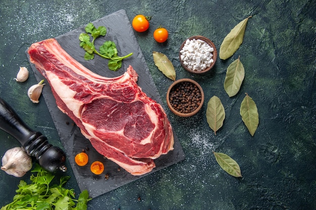 Top view big meat slice raw meat with pepper and greens on dark surface