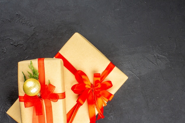 Top view big and small xmas gifts in brown paper tied with red ribbon ball on dark surface