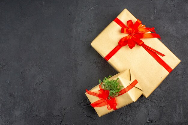 Top view big and small xmas gifts in brown paper tied with red ribbon branch fir on dark background free space