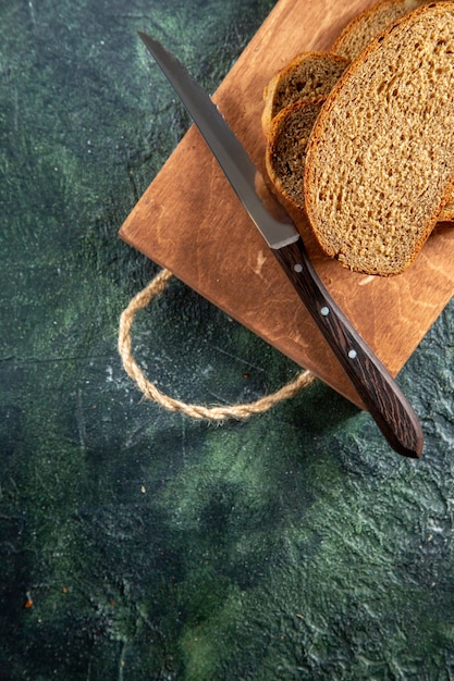 Top view of black bread knife on brown wooden cutting board on dark surface