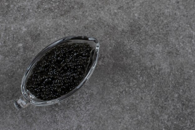 Top view of black caviar. Caviar in glass bowl over grey table.