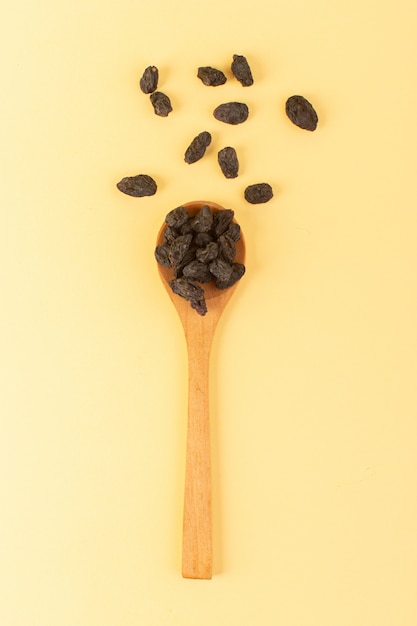 A top view black dried fruits inside brown wooden spoon isolated a top view on the cream colored