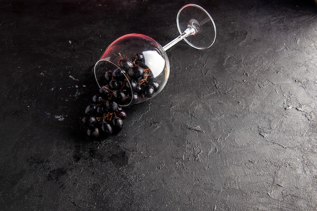 Top view black grapes in overturned wine glass on dark background