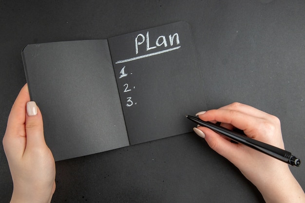 Top view black notebook and pen in female hand on black surface