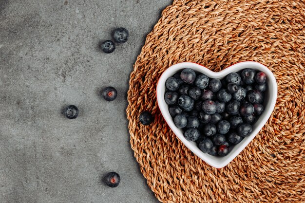 Top view black olives in heart shaped bowl on rattan trivet and gray background. horizontal