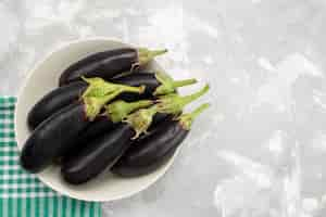 Free photo top view black raw eggplants inside white plate on the light background vegetables fresh raw food meal tree