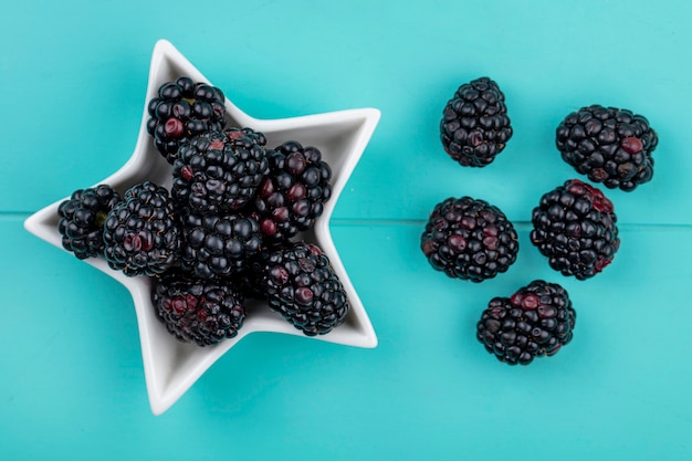 Top view of blackberry in a saucer in the form of a star on a light blue surface