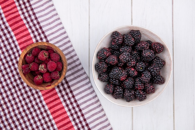 Free photo top view of blackberry with raspberries in a bowl on a red checkered towel on a white surface